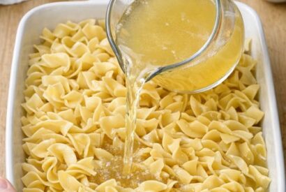 Thumbnail for Pour chicken broth over dry egg noodles, coupled with 2 ingredients, into a ceramic baking dish for a buttery side that disappears faster than anything else