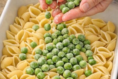 Thumbnail for Scatter frozen green peas over raw dry shell pasta, paired with these 3 ingredients, into a ceramic baking dish for a creamy dinner that’s the one e